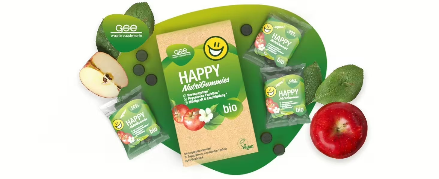 Eine Schachtel GSE Bio-Nahrungsergänzungsmittel Happy Nutragummies mit drei einzeln verpackten Gummibärchen, zwei Äpfeln, grünen Blättern und kleinen schwarzen Gummibärchen auf grün-weißem Hintergrund.