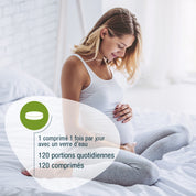 Eine schwangere Frau lächelt auf einem Bett und hält ihren Bauch. Text-Highlights Folsäure Compact (Bio) FR von gse.organic.supplements: "1 comprimé 1 fois/jour avec un verre d'eau. 120 Portionen quotidiennes. 120 comprimés.