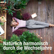 Eine lächelnde Frau liegt auf einem Holzboden mit Grünpflanzen, Obst, einem Laptop und dem Meno Wohlfühl Paket von gse organic supplements. Der deutsche Text lautet: Natürlich harmonisch durch die Wechseljahre.