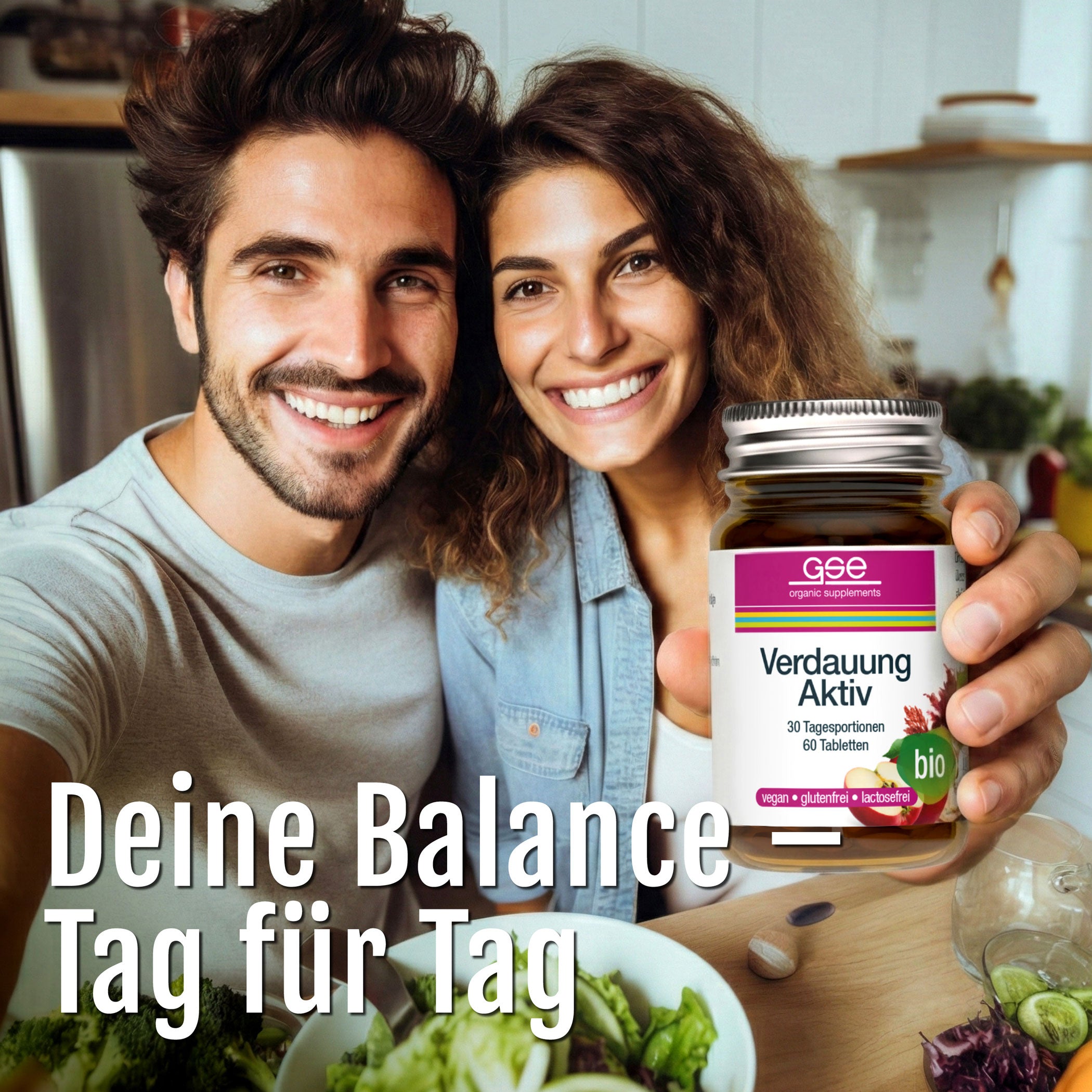 Ein lächelnder Mann und eine lächelnde Frau machen ein Selfie in einer Küche, während die Frau Verdauung Aktiv (Bio), ein Verdauungsergänzungsmittel, in der Hand hält. Frisches Gemüse liegt auf der Theke. Text: Deine Balance - Tag für Tag.