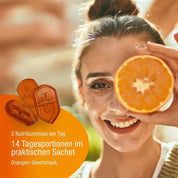 Eine lächelnde Frau hält eine halbe Orange vor ihr Auge. Links sind drei Vitamin-C-reiche Immun NutriGummies (Bio) von gse.organic.supplements abgebildet, mit deutschem Text zur täglichen Portionsbeutel und leckerem Orangengeschmack.