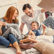Eine fröhliche vierköpfige Familie genießt eine Kissenschlacht in einem sonnendurchfluteten Schlafzimmer, umgeben von der Frische pflanzlicher Zutaten wie Grapefruit-Extrakt – genau wie die Essenz in CitroPlus® 800 (Bio) von gse.organic.supplements.