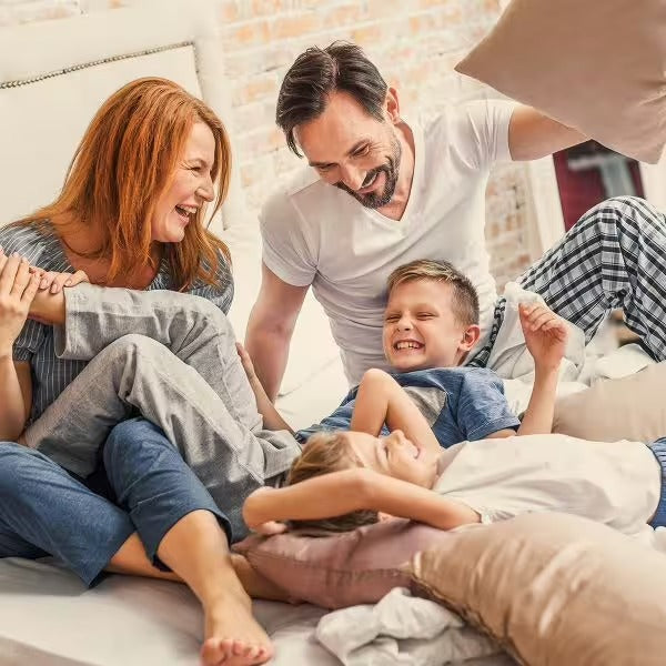 Eine fröhliche vierköpfige Familie genießt eine Kissenschlacht in einem sonnendurchfluteten Schlafzimmer, umgeben von der Frische pflanzlicher Zutaten wie Grapefruit-Extrakt – genau wie die Essenz in CitroPlus® 800 (Bio) von gse.organic.supplements.